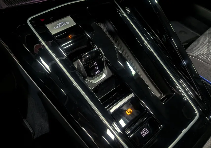 Gros plan sur la console centrale noire brillante de la Volkswagen Golf 1.5 eTSI R-Line avec levier de vitesses automatique et boutons start/stop.