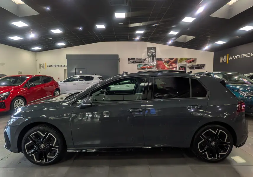 Profil côté gauche d'une Volkswagen Golf 1.5 eTSI R-Line gris dauphin avec jantes noires et toit ouvrant en showroom.