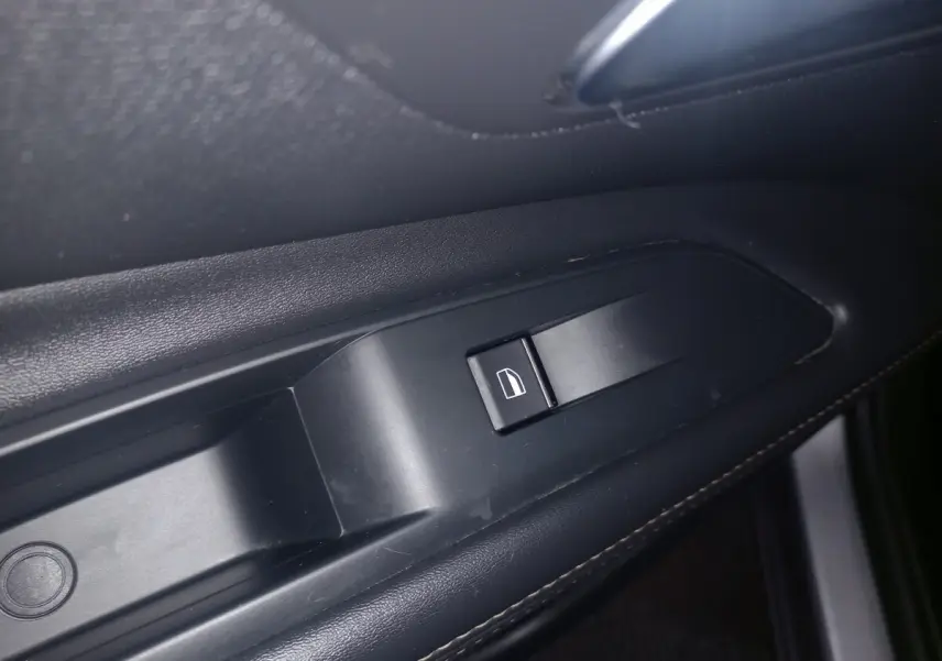 Gros plan sur le bouton de commande de la vitre électrique côté gauche, intérieur noir du Peugeot 3008 gris clair.