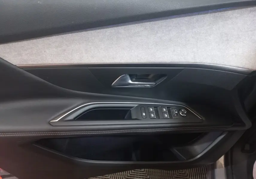 Vue intérieure côté gauche de la porte avant d’un Peugeot 3008 gris clair, avec commandes électriques et poignée chrome.