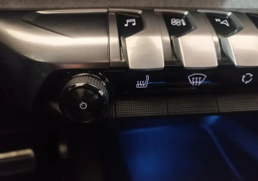 Gros plan sur les commandes argentées et noires du tableau de bord du Peugeot 3008 gris clair, avec éclairage bleu dessous.