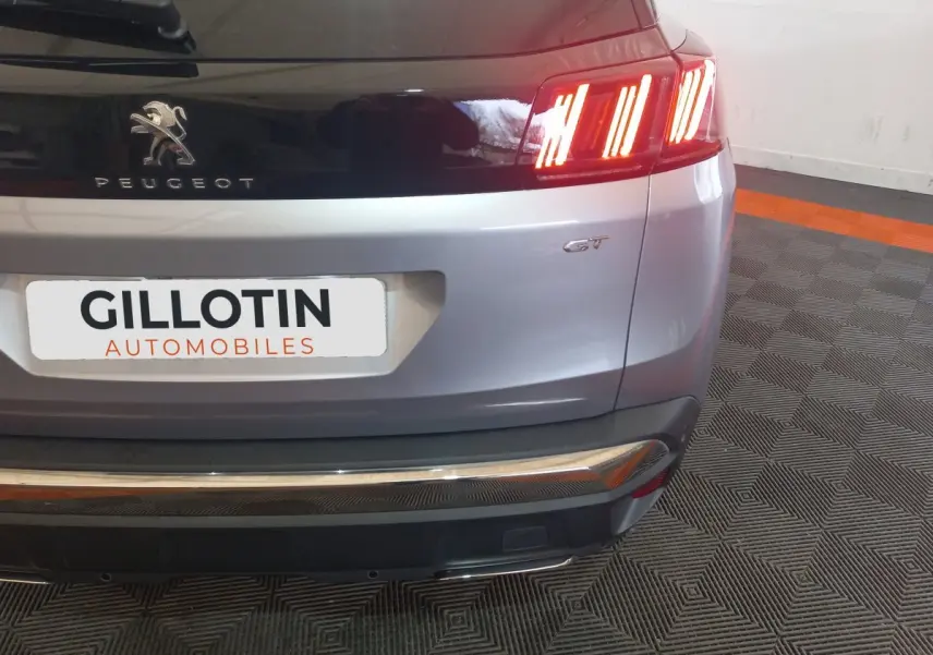 Vue arrière droite du Peugeot 3008 GT gris clair avec feux LED allumés et logo distinctif GT visible.