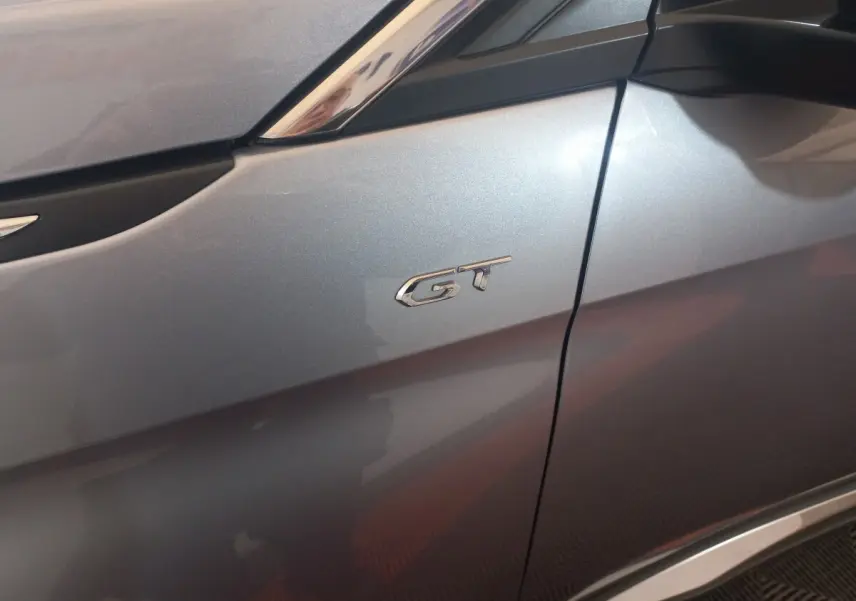 Gros plan sur l’aile avant gauche gris clair d’un Peugeot 3008 GT avec logo GT chromé visible.