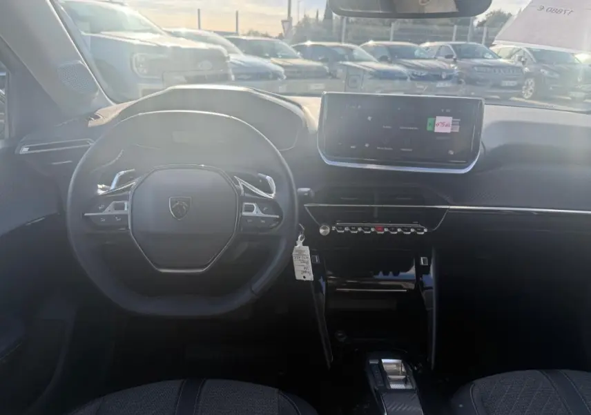 Vue intérieure frontale du poste de conduite de la Peugeot 208 Hybrid 110 e-DCS6 Allure 2024 avec écran tactile et volant compact noir.
