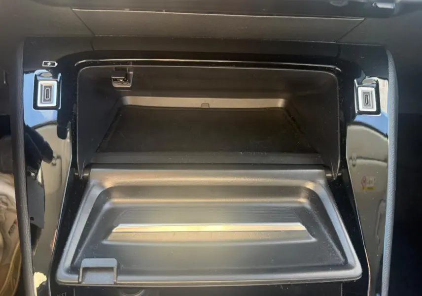 Vue rapprochée de la console centrale noire du Peugeot 208 Hybrid 110 e-DCS6 Allure 2024, avec compartiment ouvert.