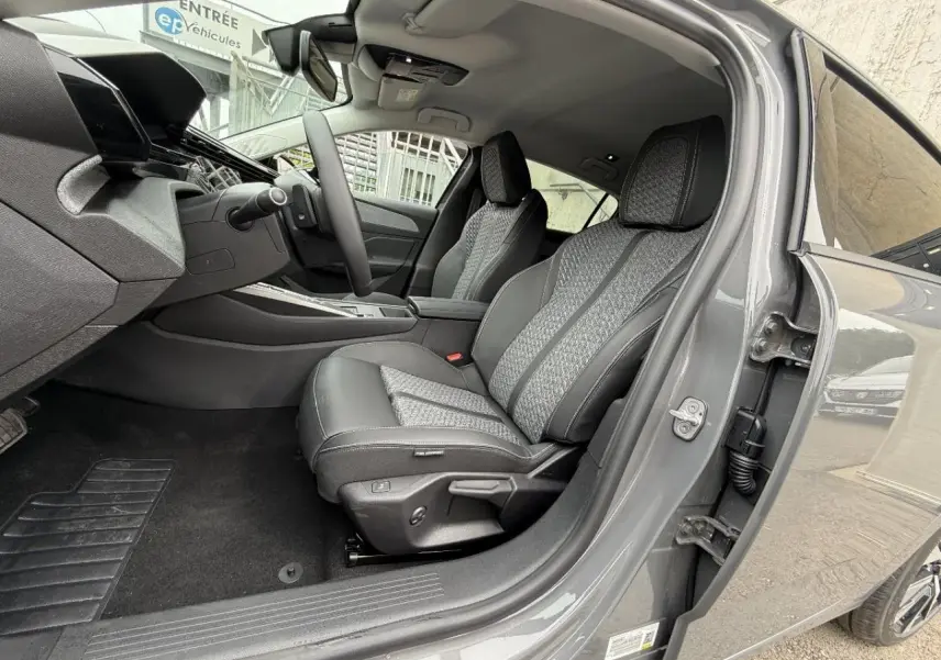 Intérieur côté conducteur du Peugeot 308 gris sélénite 2026, sièges tissu et cuir avec surpiqûres contrastées visibles.