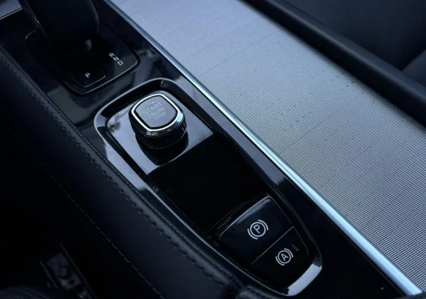 Gros plan sur la console centrale noire du Volvo XC90 2024, avec bouton Start/Stop et frein à main électronique.
