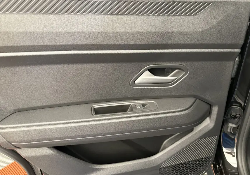 Intérieur côté gauche de la porte avant noire du Dacia Duster 2025 avec poignée et commande de vitre électrique.