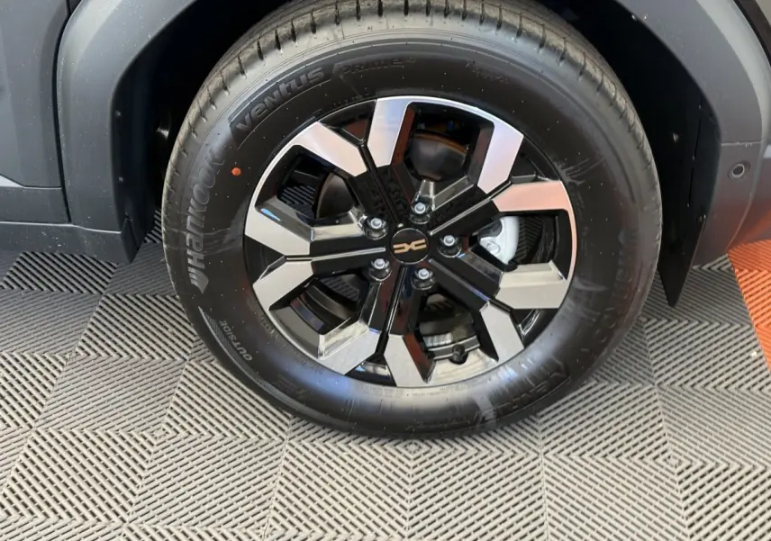 Gros plan sur la roue avant droite du Dacia Duster noir 2025 avec jante alliage bicolore et pneu Hankook.