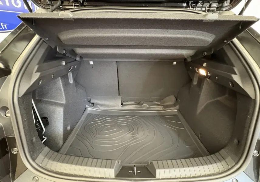Coffre ouvert noir du Dacia Duster 2025 hybride, vue intérieure montrant tapis de protection et éclairage latéral.