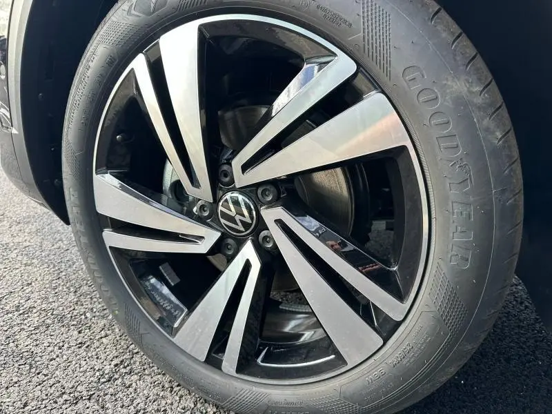 Gros plan sur la jante noire et argentée du Volkswagen T-Roc gris 2025 avec logo VW au centre et pneu Goodyear visible.