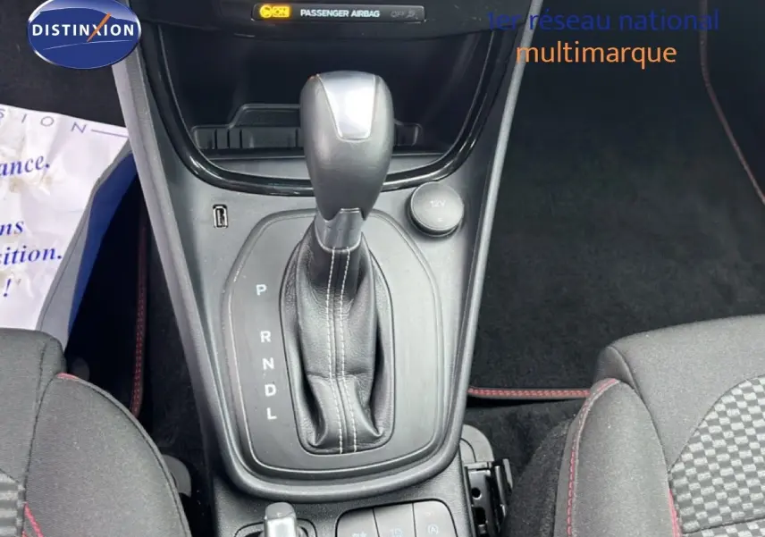 Le levier de vitesses automatique en cuir noir du Ford Puma 2024, avec console centrale et sièges tissu gris à surpiqûres rouges.
