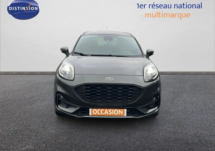 Vue frontale d'un Ford Puma gris magnétique 2024 avec calandre noire et phares allumés sur fond neutre.