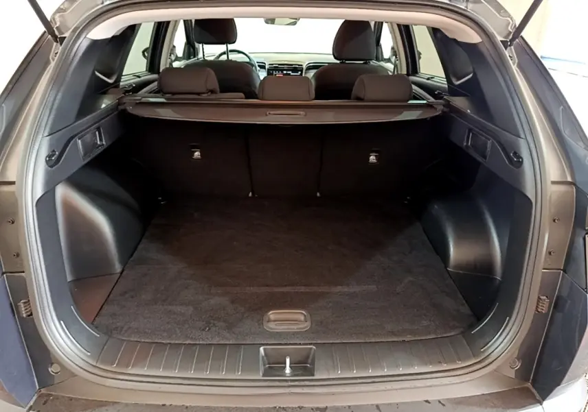 Coffre ouvert vu de l'arrière d'un Hyundai Tucson gris foncé, avec banquette arrière et cache-bagages visibles.