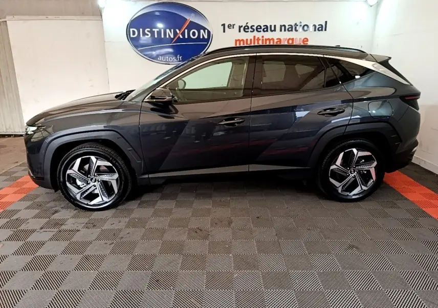 Vue de profil côté gauche d'un Hyundai Tucson gris foncé 2022 avec jantes alliage et toit noir dans un showroom.