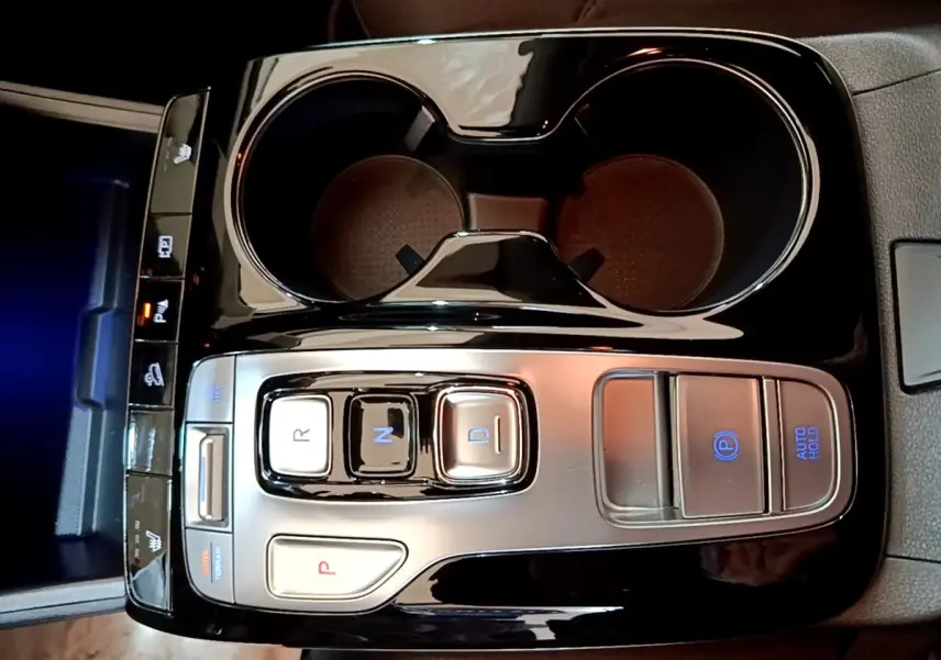 Vue plongeante sur la console centrale noire du Hyundai Tucson 1.6 PHEV 265 HTRAC avec commandes de boîte auto et porte-gobelets.