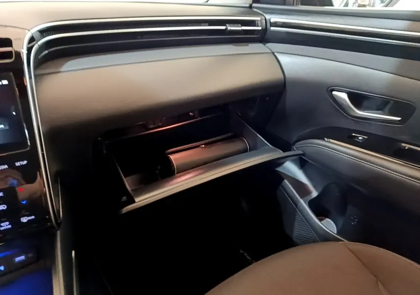Intérieur Hyundai Tucson 2022 vue côté passager, boîte à gants ouverte, tableau de bord noir moderne avec écran tactile partiel visible.