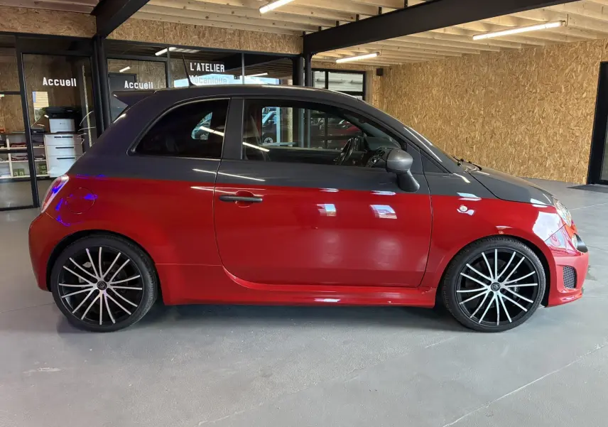 Profil droit d'une Abarth 500 Competizione 2016 rouge et gris avec jantes noires à rayons fins, en intérieur d'atelier.