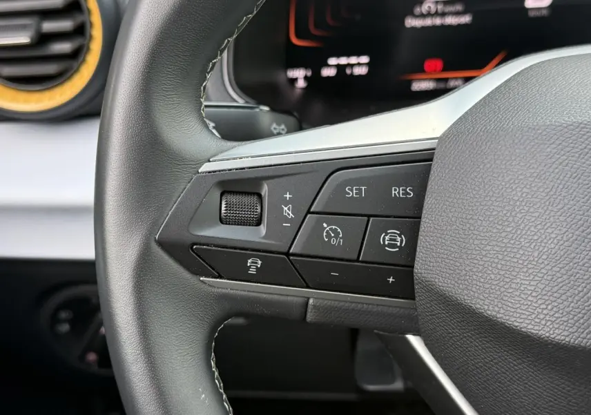 Gros plan sur les commandes du volant à gauche du SEAT Arona TSI 115 Style 2025, intérieur noir avec détails argentés.
