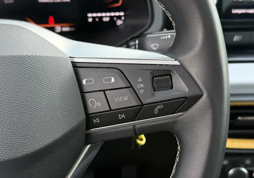 Gros plan sur les commandes au volant à gauche du SEAT Arona 2025, finition Style, avec tableau de bord digital en arrière-plan.