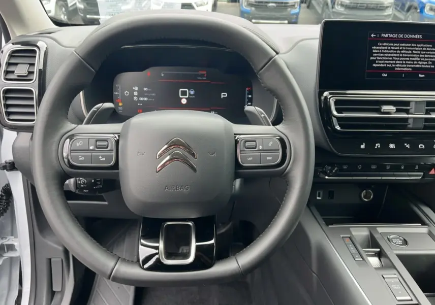 Vue intérieure centrée sur le volant cuir multifonctions et tableau de bord digital du Citroën C5 Aircross blanc okénite.