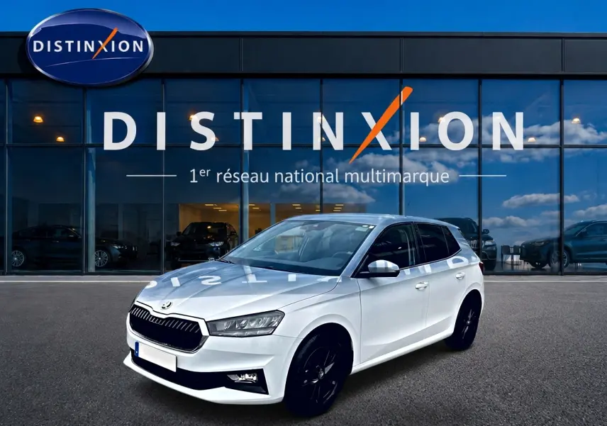 SKODA FABIA blanche vue 3/4 avant droit, jantes noires, devant vitrine Distinxion reflet ciel bleu.