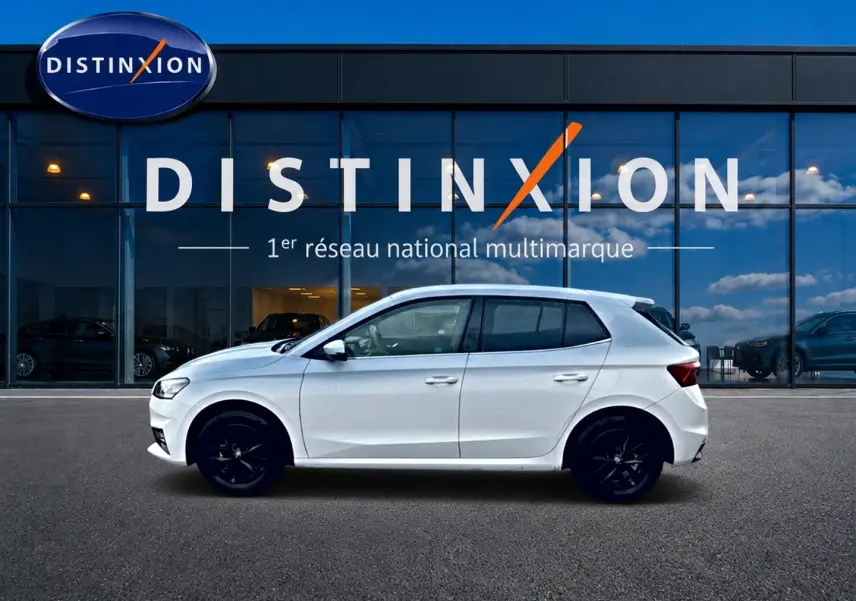 Profil droit d'une Skoda Fabia blanche 2025 avec jantes noires, garée devant une vitrine Distinxion.