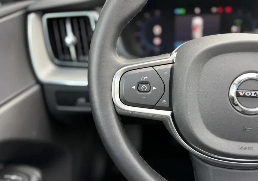 Gros plan sur le volant simili-cuir gris du Volvo XC60 T6 AWD PHEV 2024, avec commandes de régulateur de vitesse.