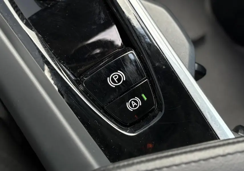 Gros plan sur les commandes du frein de parking et de l'arrêt automatique dans le console centrale noire du Volvo XC60 gris Silver 2024.