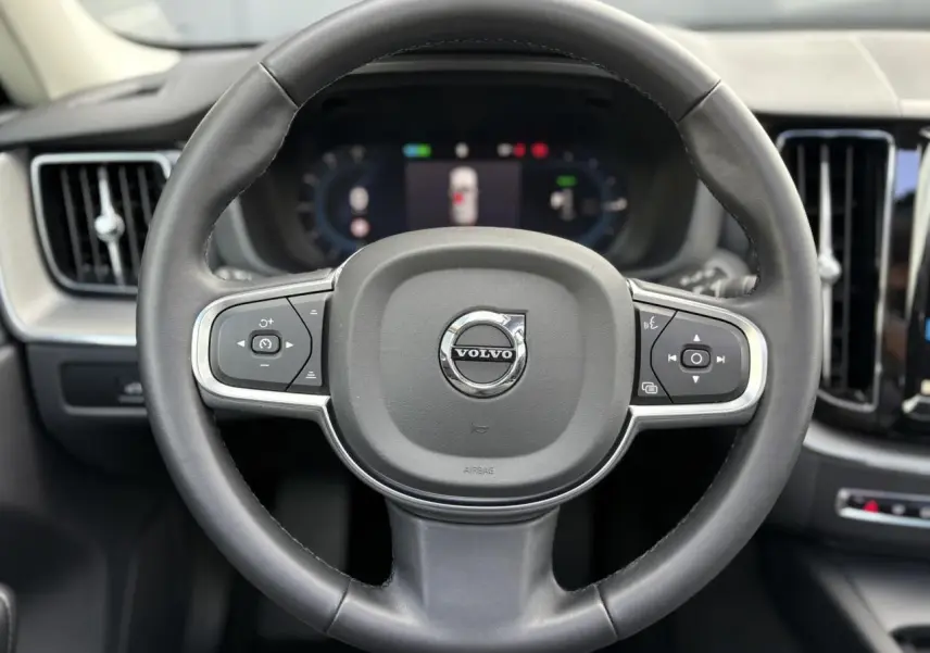 Volant simili-cuir noir de Volvo XC60 2024 avec commandes intégrées et tableau de bord digital en arrière-plan.