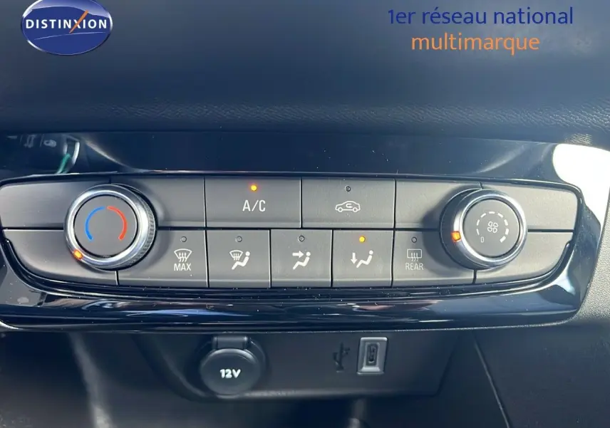 Gros plan sur la console de climatisation de l'Opel Corsa gris Kristal Metal, avec commandes et prise 12V visibles.