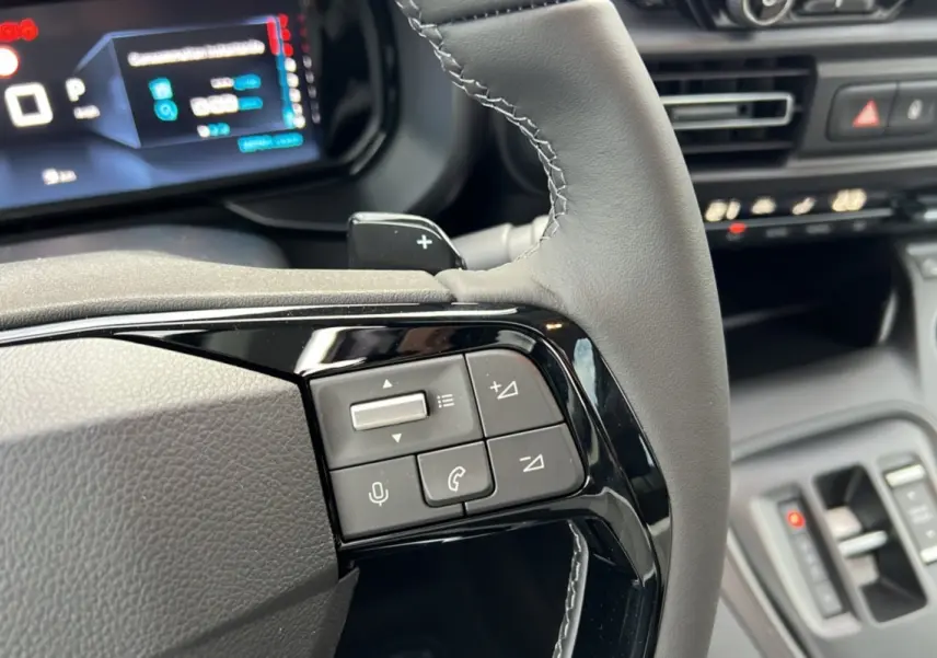 Gros plan sur les commandes au volant du Citroën Berlingo 2025 noir perla nera, avec tableau de bord numérique en arrière-plan.