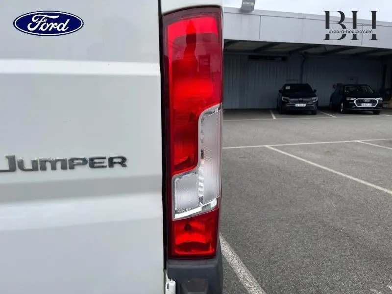 Gros plan sur le feu arrière droit blanc et rouge du Citroën Jumper blanc banquise, avec logo et parking en arrière-plan.