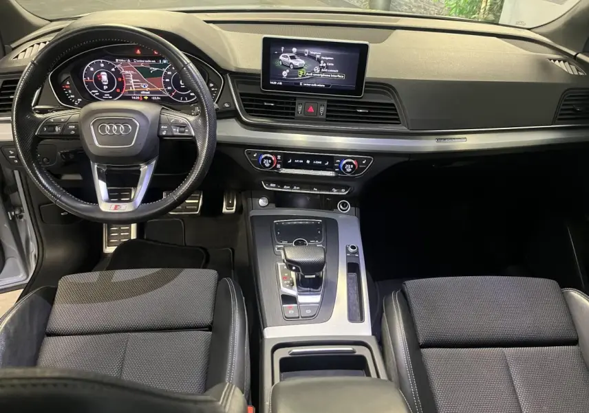 Intérieur Audi Q5 S line 2019 vu de face, volant cuir perforé, écran central et console avec boîte auto gris.