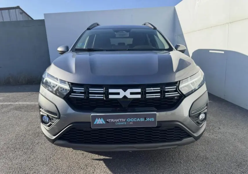 Vue frontale d'un Dacia Jogger gris schiste métallisé avec calandre noire et feux LED allumés.