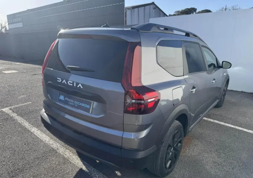 Vue 3/4 arrière droit d'un Dacia Jogger gris schiste métal avec barres de toit et feux arrière LED distinctifs.