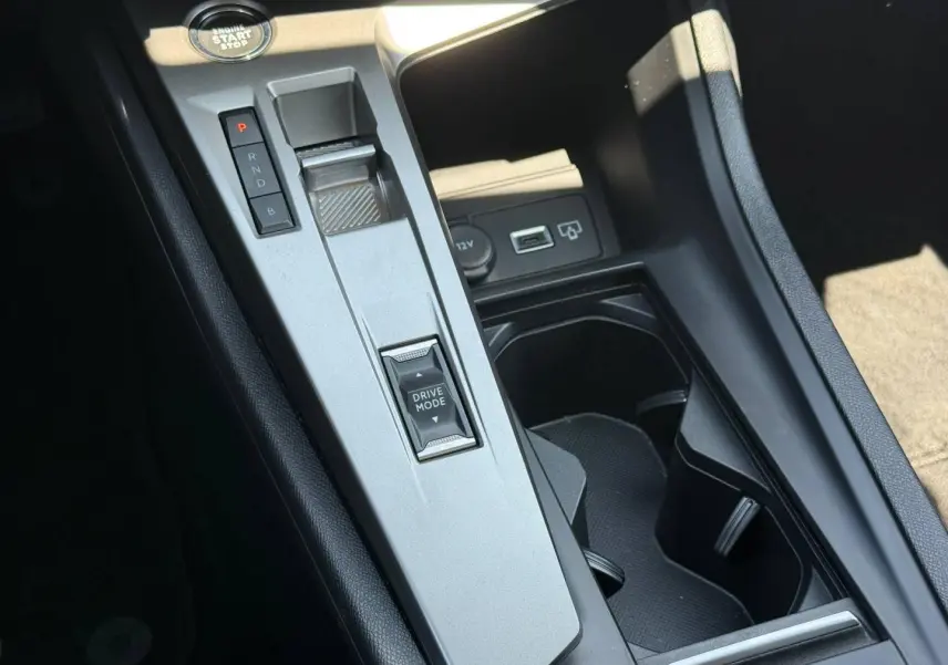 Gros plan sur la console centrale argentée de la Peugeot e-308 noire, avec levier de vitesses et bouton Drive Mode.