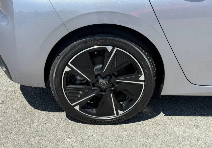 Gros plan sur la roue arrière droite de la Peugeot e-308 2025 gris clair avec jante alu noire et argentée au design géométrique.
