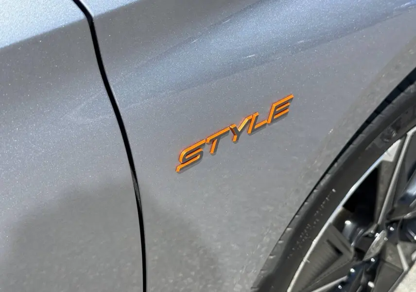 Gros plan sur l’inscription orange "STYLE" sur l’aile avant droite d’une Peugeot 308 e-308 noir Perla Nera.