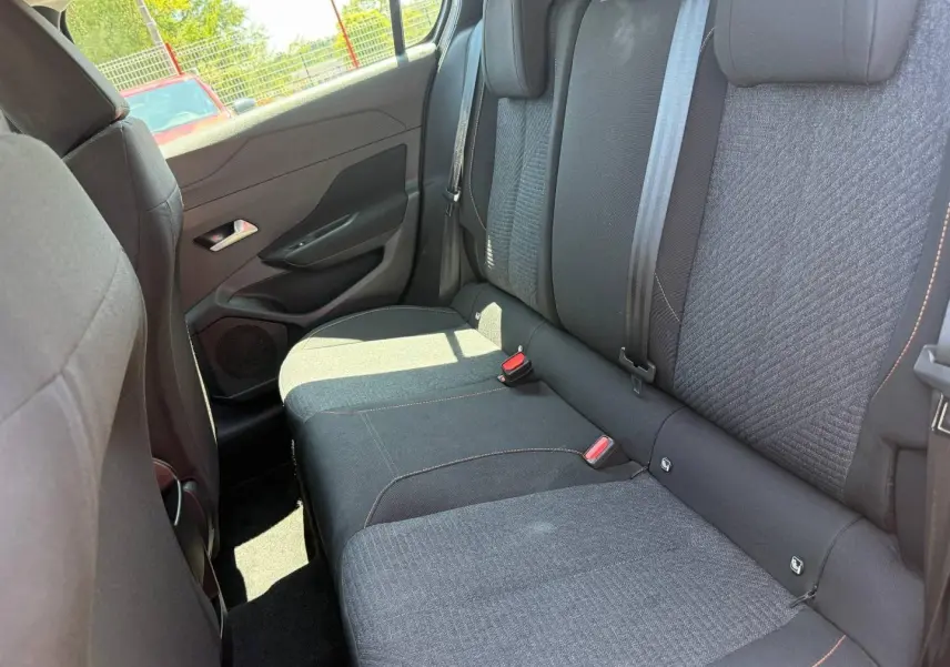 Vue intérieure côté droit montrant la banquette arrière en tissu noir avec surpiqûres orange de la Peugeot 308 e-308 2025.