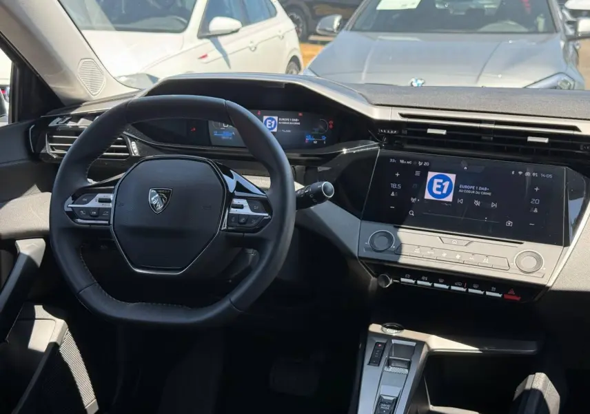 Vue intérieure avant de la Peugeot 308 e-308 noire, volant multifonction et écran tactile central lumineux.
