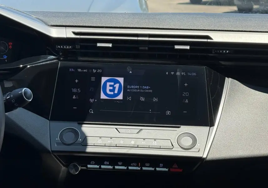 Vue rapprochée de la console centrale tactile noire de la Peugeot e-308 2025 avec commandes climatisation et radio numérique.