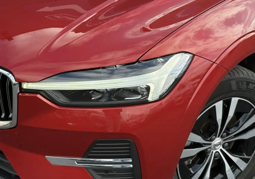 Gros plan sur l'avant droit du Volvo XC60 rouge Fusion, mettant en valeur le phare LED et la jante alliage 18 pouces.