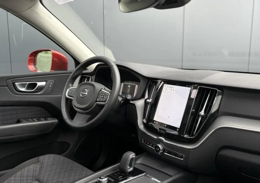 Vue intérieure côté conducteur du Volvo XC60 rouge Fusion 2024, avec tableau de bord moderne et écran tactile vertical.