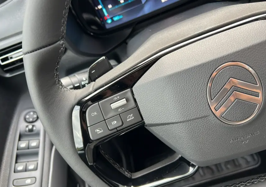 Gros plan sur le volant cuir du Citroën Berlingo 2025 avec commandes intégrées et logo chromé au centre.