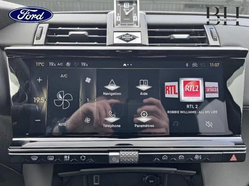 Vue rapprochée de l’écran tactile central noir brillant du DS7 2023 avec horloge analogique et commandes climatisation visibles.