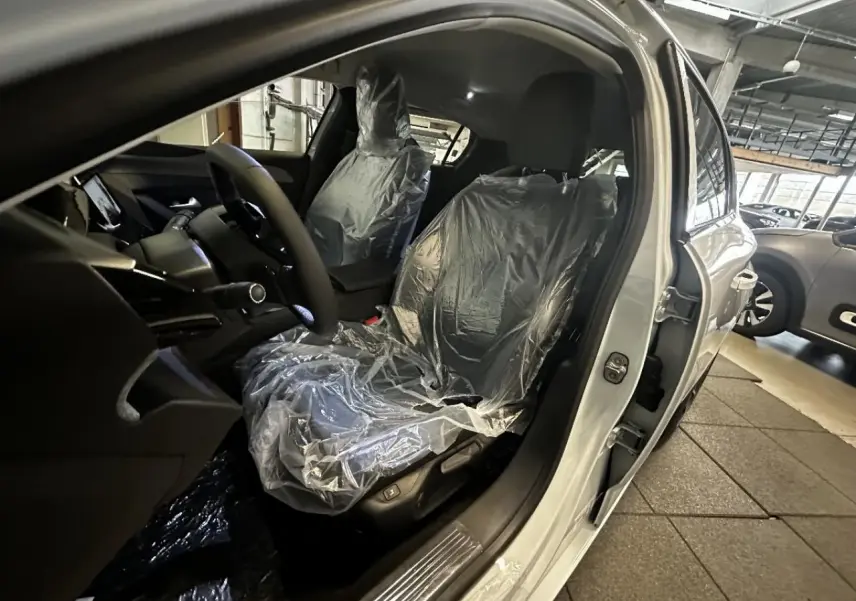 Vue intérieure côté conducteur de la Peugeot 308 blanc okenite 2024, sièges protégés par housses plastiques.