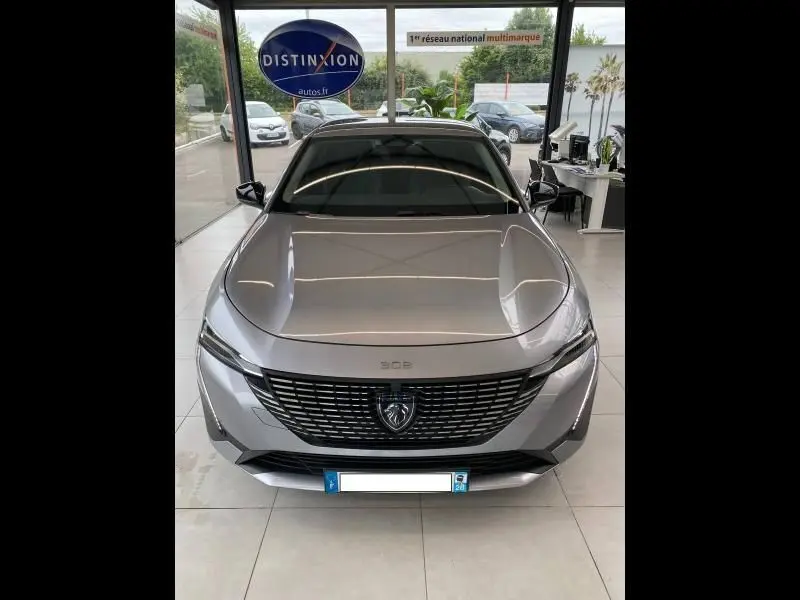 Vue de face d'une Peugeot 308 gris Artense exposée en showroom avec sa calandre distinctive et ses phares LED fins.