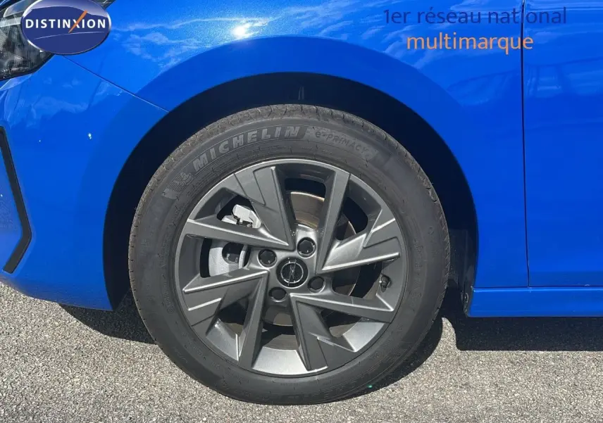 Gros plan sur la roue avant gauche d'une Opel Corsa bleu voltaik métal avec jante alliage gris foncé.