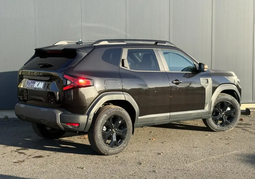 Vue 3/4 arrière droite du Dacia Duster 2026 noir nacré avec jantes alliage noires et barres de toit longitudinales.